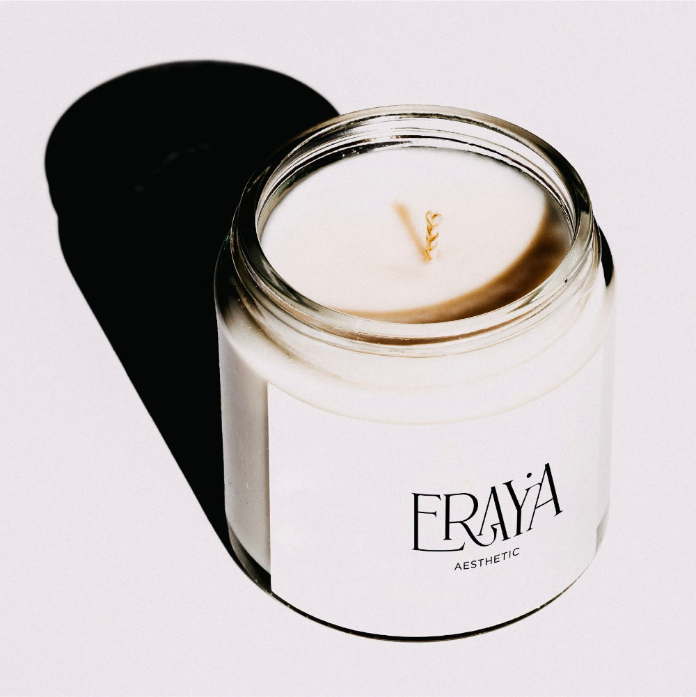 Candle in a glass jar with a white label featuring 'Fraya Aesthetic' on a light gray background.