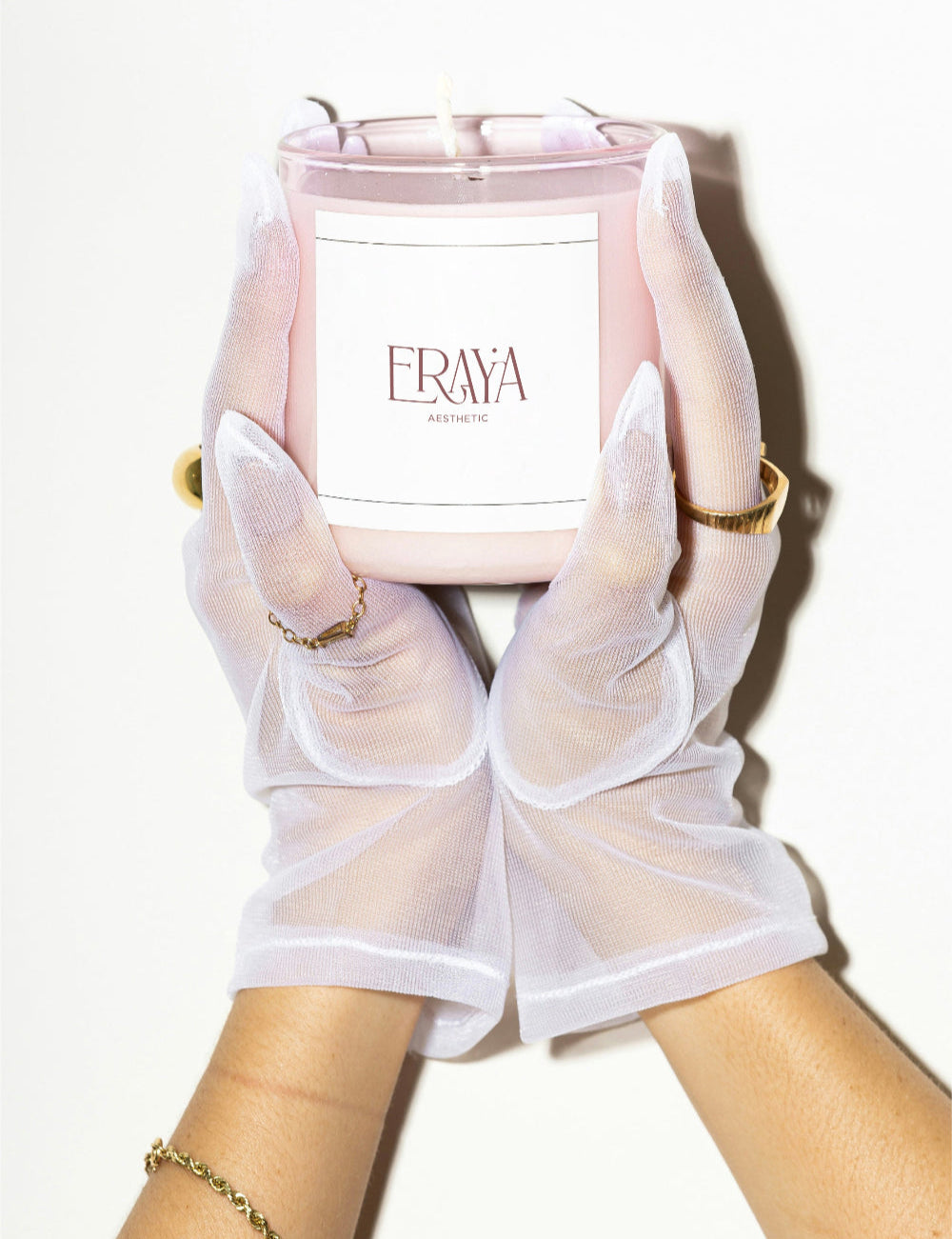 Candle with 'Eraya' branding held by hands wearing white gloves on a white background